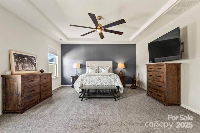 carpeted bedroom with a ceiling fan, a raised ceiling, visible vents, and baseboards