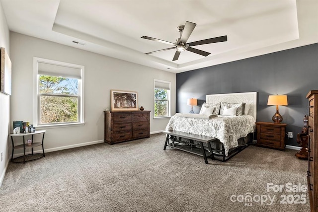 carpeted bedroom with visible vents, a tray ceiling, and baseboards