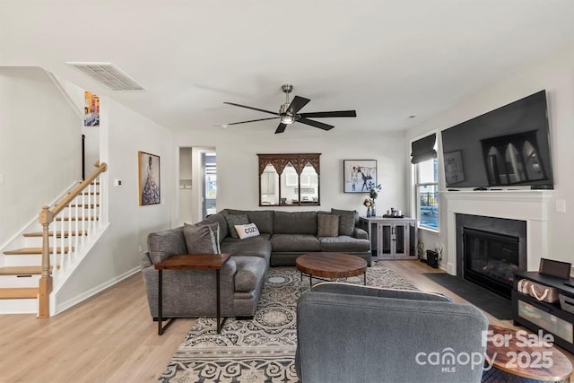 living room featuring visible vents, stairway, light wood-style floors, a fireplace with flush hearth, and baseboards