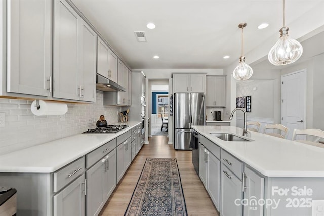 kitchen featuring stainless steel appliances, visible vents, gray cabinetry, a sink, and under cabinet range hood