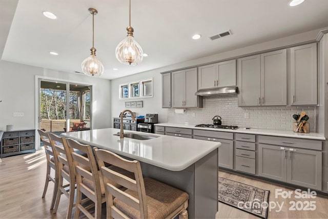 kitchen with under cabinet range hood, a sink, visible vents, gray cabinets, and stainless steel gas stovetop