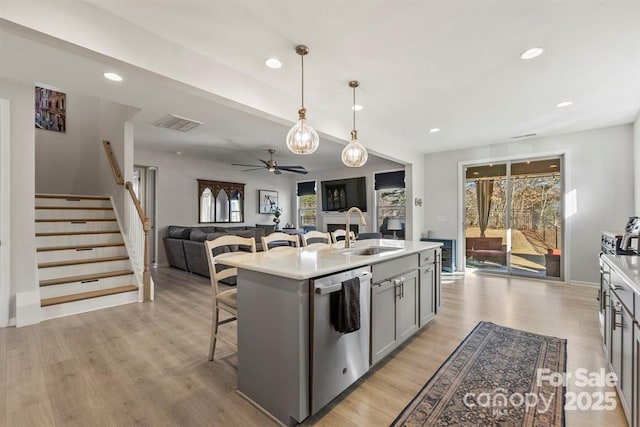 kitchen featuring a sink, a kitchen breakfast bar, light countertops, stainless steel dishwasher, and gray cabinets