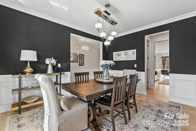 dining space with a wainscoted wall, light wood-type flooring, a notable chandelier, and crown molding