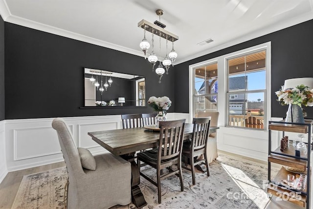 dining area featuring ornamental molding, wainscoting, visible vents, and wood finished floors