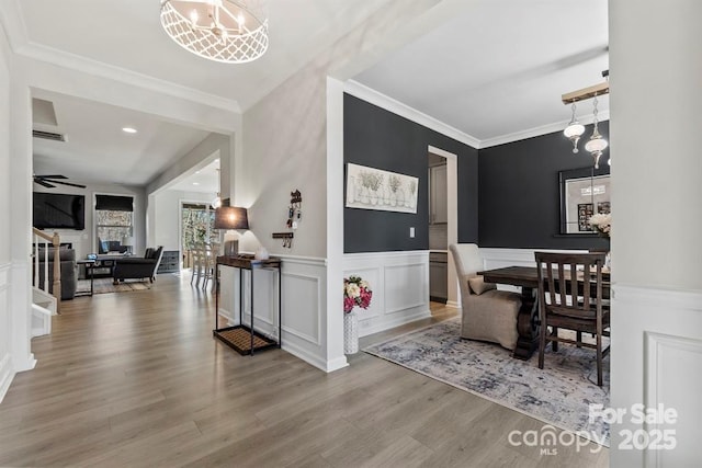 dining room with stairs, crown molding, wainscoting, wood finished floors, and ceiling fan with notable chandelier