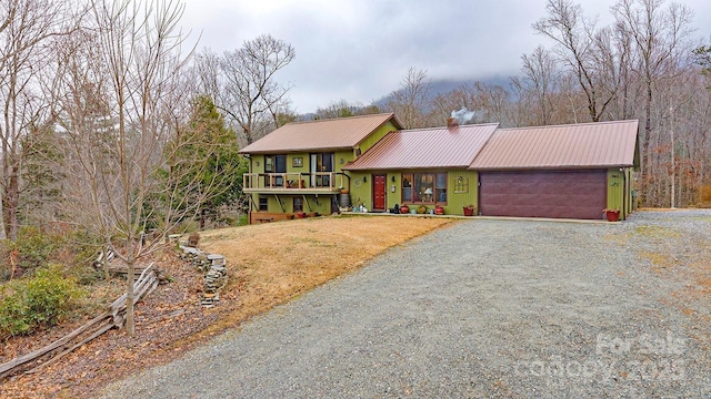 view of front facade featuring a garage, a chimney, metal roof, gravel driveway, and a front lawn