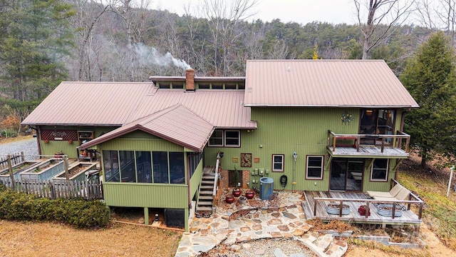 view of front of property featuring metal roof, a wooded view, a sunroom, and central air condition unit