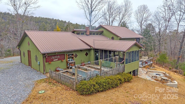 view of front of house featuring gravel driveway, a vegetable garden, a sunroom, metal roof, and a forest view