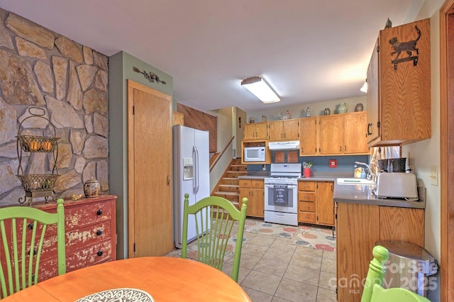 kitchen featuring brown cabinets, light tile patterned flooring, a sink, white appliances, and under cabinet range hood