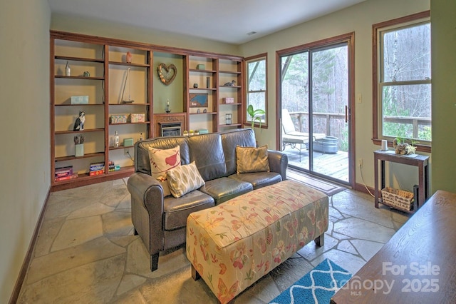 living area with baseboards, stone tile flooring, and a glass covered fireplace