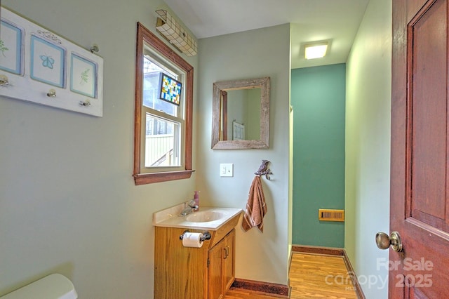 half bath with visible vents, baseboards, toilet, wood finished floors, and vanity