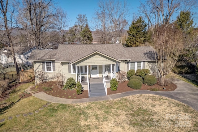 view of front of home featuring covered porch, a shingled roof, fence, driveway, and a front yard