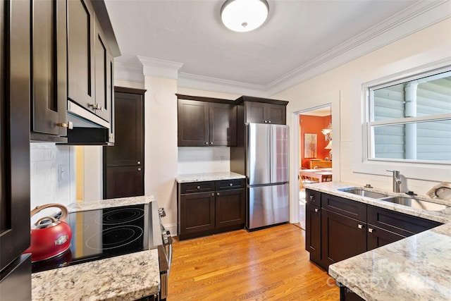 kitchen featuring light wood finished floors, freestanding refrigerator, a sink, dark brown cabinets, and range with electric cooktop