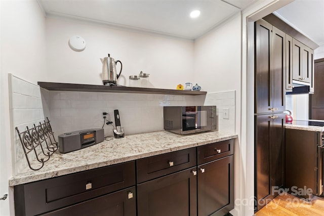 kitchen featuring dark brown cabinets, decorative backsplash, light stone countertops, open shelves, and crown molding