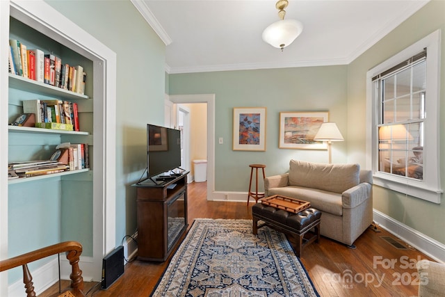 living area with baseboards, crown molding, visible vents, and hardwood / wood-style floors