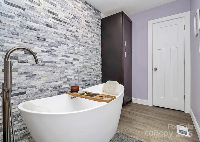 bathroom with a soaking tub, wood finished floors, visible vents, and baseboards