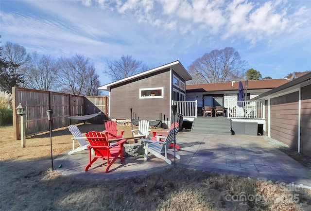 rear view of property featuring a fire pit, a patio, a deck, and fence