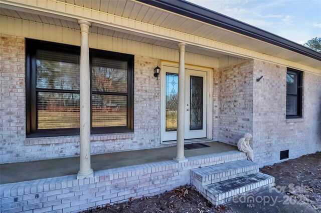 doorway to property featuring brick siding, crawl space, and a porch