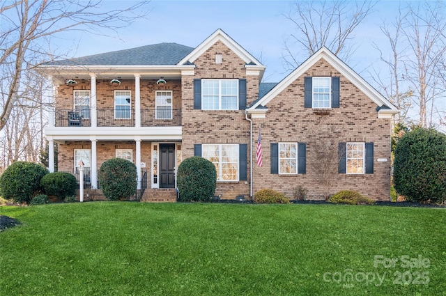 view of front of house featuring a balcony, roof with shingles, a front lawn, and brick siding