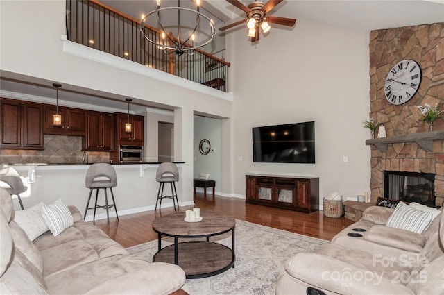 living room with a towering ceiling, a stone fireplace, baseboards, and wood finished floors