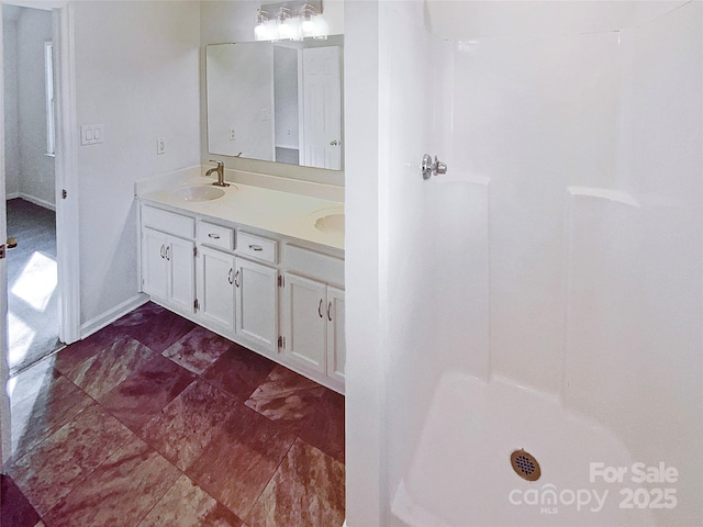 full bath featuring a shower, a sink, baseboards, and double vanity