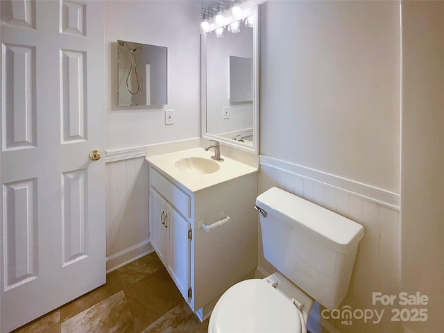 bathroom with toilet, vanity, a decorative wall, and wainscoting