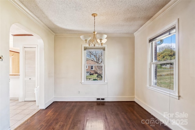 unfurnished dining area with visible vents, arched walkways, ornamental molding, wood finished floors, and an inviting chandelier