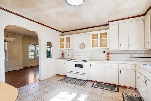 kitchen featuring arched walkways, electric stove, glass insert cabinets, crown molding, and white cabinetry