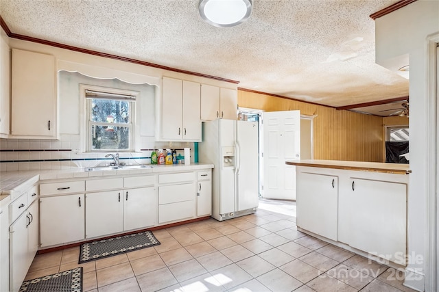 kitchen with a ceiling fan, tile countertops, crown molding, white fridge with ice dispenser, and a sink