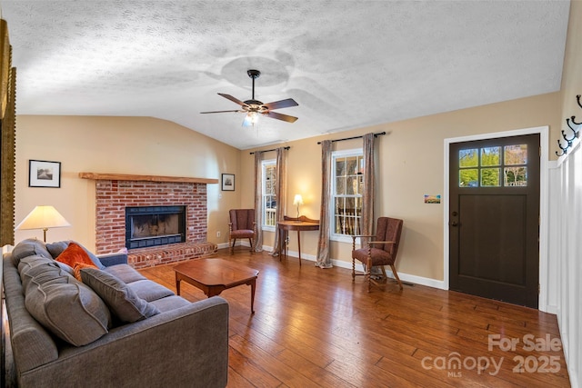 living area with lofted ceiling, hardwood / wood-style floors, a brick fireplace, a textured ceiling, and baseboards