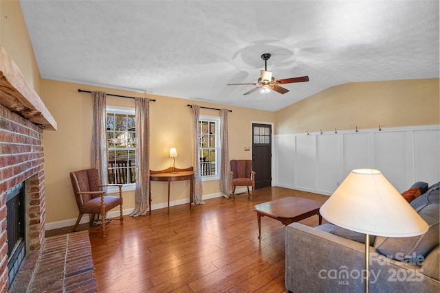 sitting room with lofted ceiling, ceiling fan, a textured ceiling, a fireplace, and wood finished floors