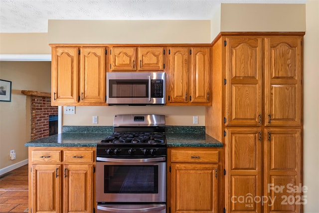 kitchen featuring stainless steel appliances, dark countertops, brown cabinetry, and a textured ceiling