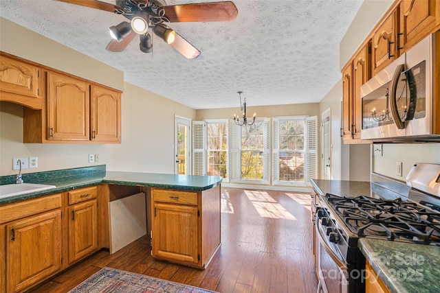 kitchen with stainless steel appliances, dark wood-type flooring, a peninsula, a sink, and dark countertops