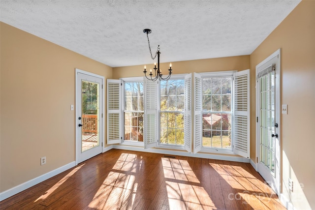 unfurnished dining area with a wealth of natural light, an inviting chandelier, baseboards, and hardwood / wood-style flooring