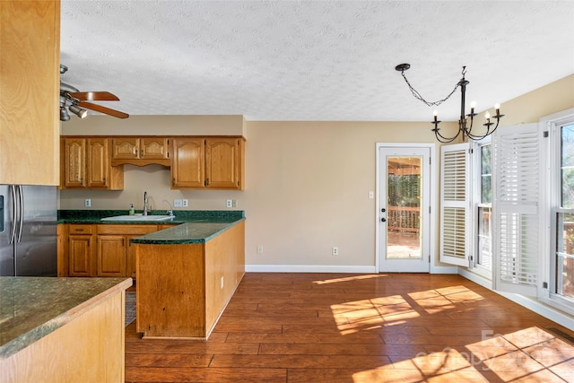 kitchen featuring a sink, freestanding refrigerator, dark wood-style floors, brown cabinetry, and dark countertops