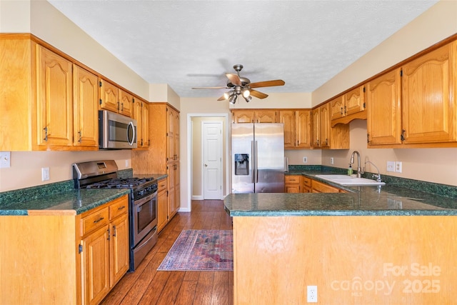 kitchen featuring stainless steel appliances, dark wood-type flooring, a peninsula, a sink, and dark countertops