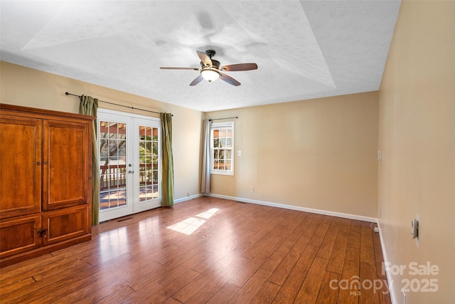 empty room featuring wood-type flooring, baseboards, a textured ceiling, and french doors