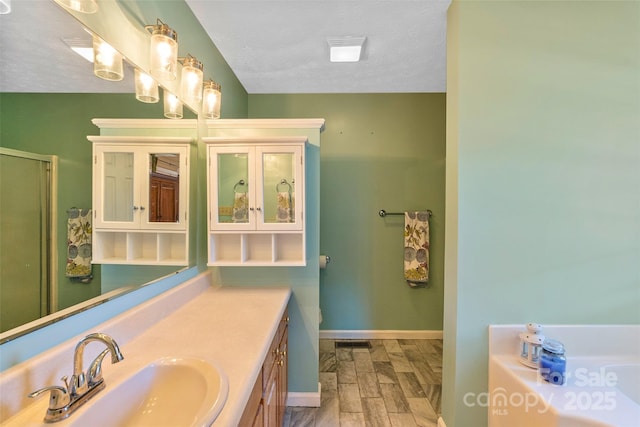 full bath featuring a textured ceiling, a garden tub, wood finish floors, vanity, and baseboards