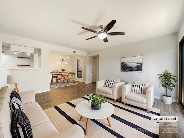 living room featuring baseboards, visible vents, wood finished floors, and ceiling fan with notable chandelier