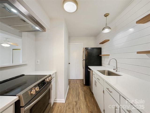 kitchen featuring appliances with stainless steel finishes, white cabinetry, a sink, light wood-type flooring, and wall chimney exhaust hood