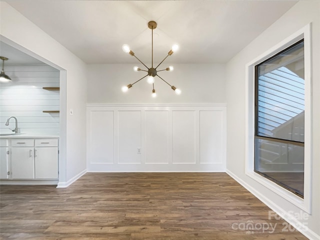 unfurnished dining area featuring dark wood-style floors, a decorative wall, a sink, and an inviting chandelier