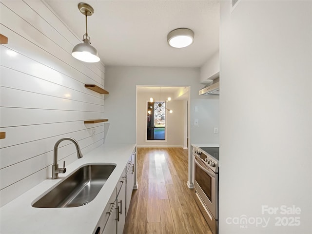 kitchen featuring open shelves, electric range, light wood-style floors, a sink, and wall chimney range hood