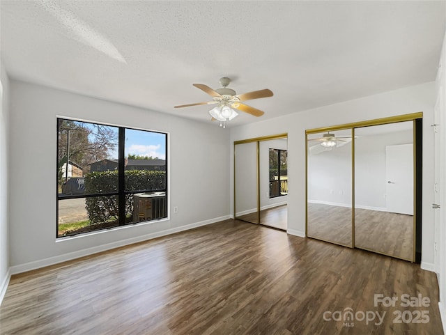 unfurnished bedroom featuring wood finished floors, a textured ceiling, baseboards, and two closets