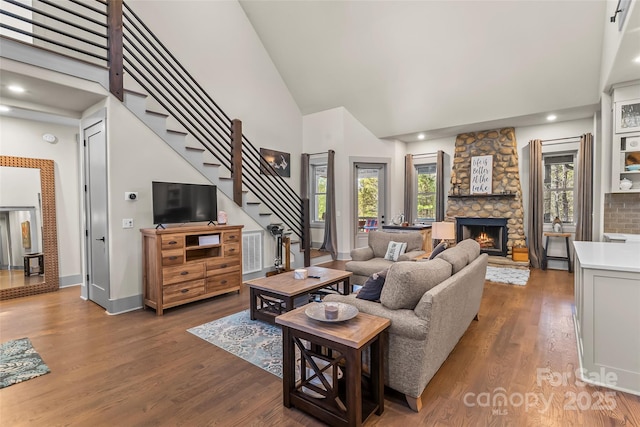 living room featuring wood finished floors, stairs, a fireplace, high vaulted ceiling, and a wealth of natural light