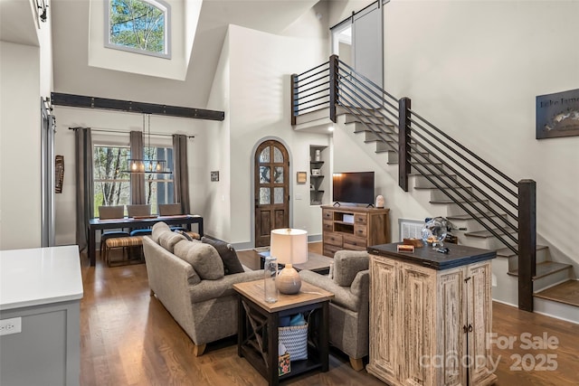 living area featuring stairs, dark wood-type flooring, and a towering ceiling