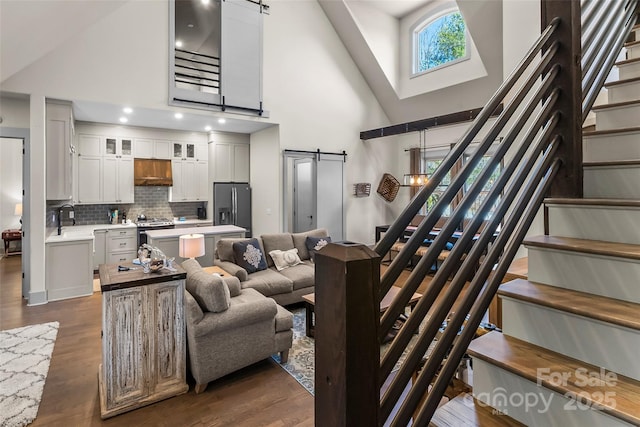 living area with stairs, high vaulted ceiling, dark wood-style floors, and a barn door