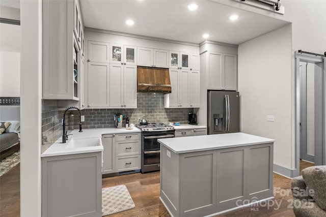 kitchen featuring stainless steel appliances, a kitchen island, a sink, backsplash, and range hood