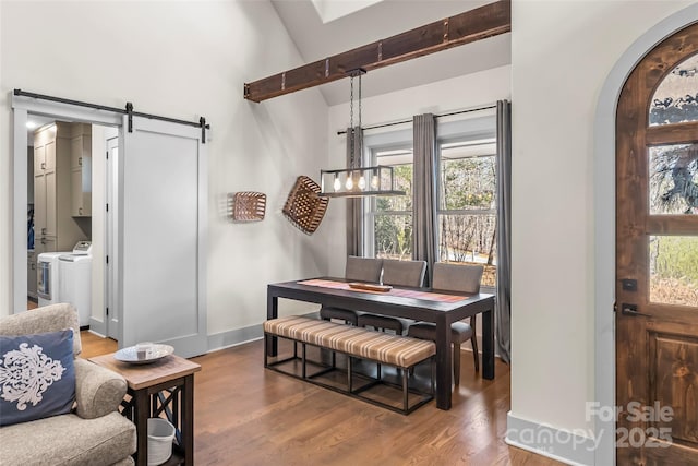 dining area with a barn door, baseboards, arched walkways, wood finished floors, and washer and dryer