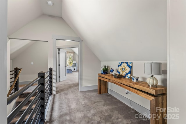 hallway with carpet, baseboards, vaulted ceiling, and an upstairs landing