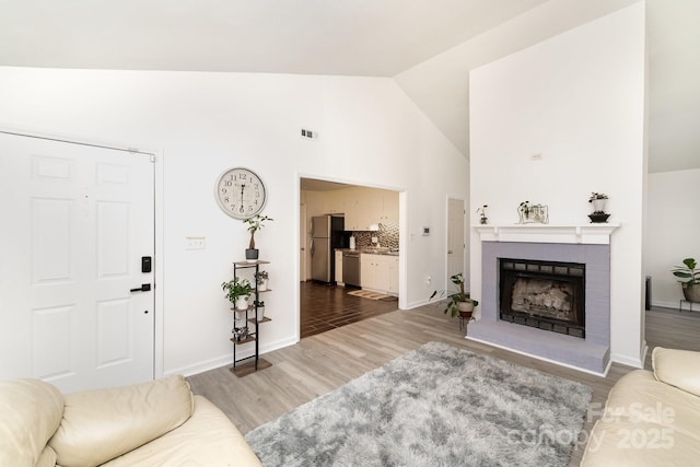 living room with visible vents, baseboards, light wood-style flooring, a fireplace, and high vaulted ceiling